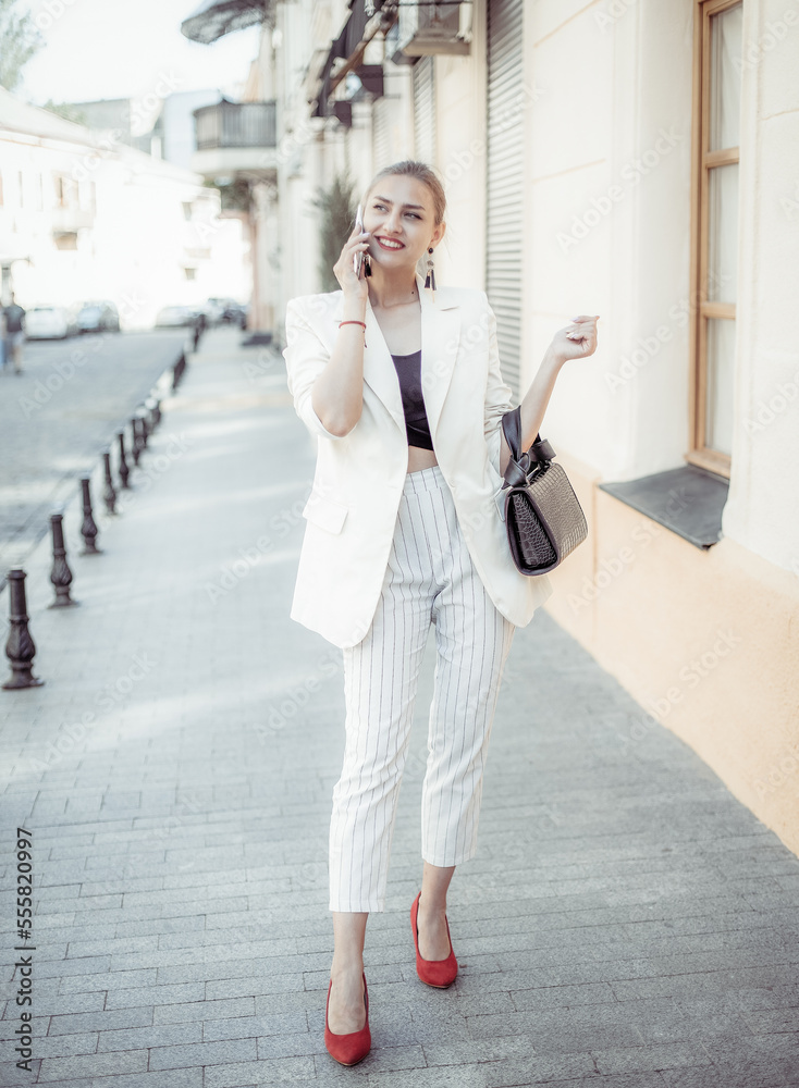 Fototapeta premium Charming smiling fashion woman talking on the phone on a european street