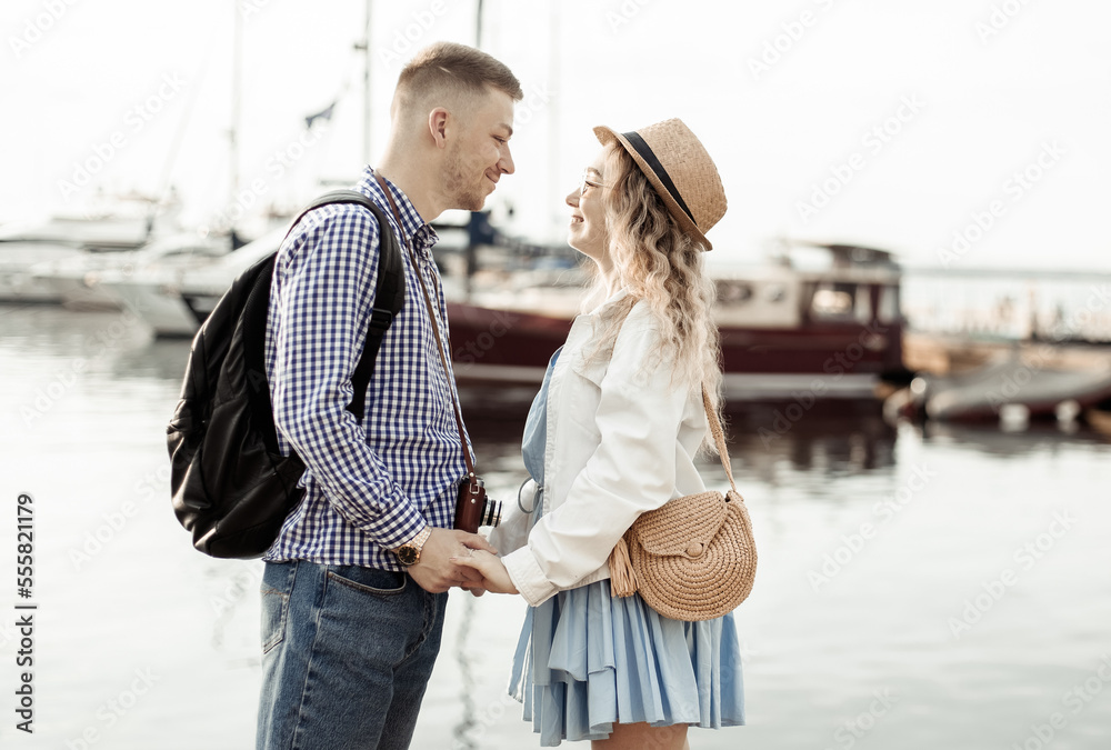 Young loving couple of tourists hold hands on the background of the yacht club. Love, travel concept