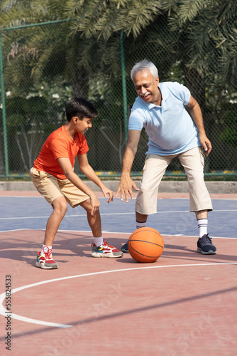 Grandfather and his grandson enjoying and playing together on basketball court. © G-images