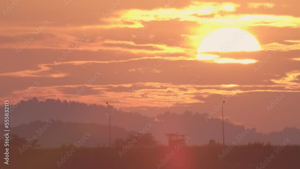Daybreak in the morning is marked by the large sun rising gradually from above the horizon. In the winter morning, the sun rises amid a hazy sky and a mountain. Dawn sunrise on the natural landscape. Daybreak in the morning is marked by the large sun rising gradually from above the horizon. In the winter morning, the sun rises amid a hazy sky and a mountain. Dawn sunrise on the natural landscape.