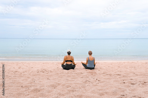 two girls are sitting in the lotus position and meditating on the sand on the beach