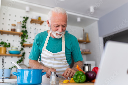 Happy senior man having fun cooking at home - Elderly person preparing health lunch in modern kitchen - Retired lifestyle time and food nutrition concept