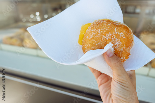 Hand holding Bola de Berlim or Berlim Ball, a Portuguese pastry made from a fried donut filled with sweet eggy cream and rolled in crunchy sugar. photo
