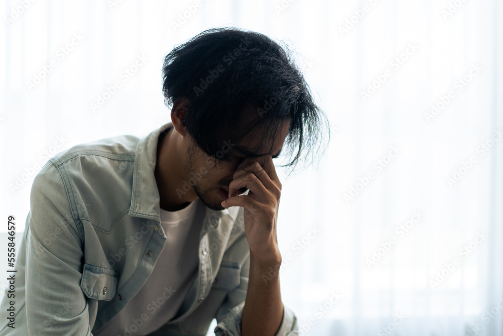 Asian young upset depressed man sitting alone in living room at home. Asian young upset depressed man sitting alone in living room at home.