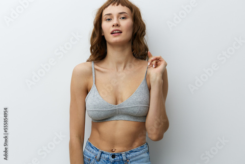 a beautiful, sexy, playful woman with tanned skin color and red hair stands on a white background playfully pulling the strap of her top