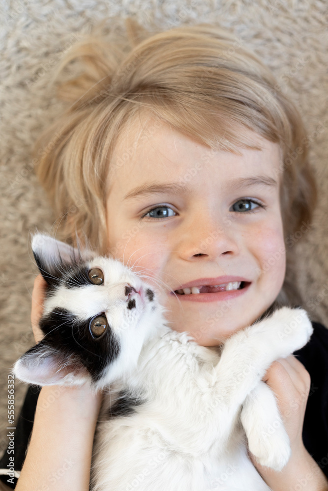 face of contented blond boy and black and white kitten. Top view, selective focus. Pets. Happy childhood. Lifestyle. care and joy from animals face of contented blond boy and black and white kitten. Top view, selective focus. Pets. Happy childhood. Lifestyle. care and joy from animals