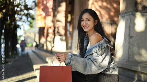 Elegant young woman holding shopping bags sitting at urban stairs with leaves shadow and sunlight 