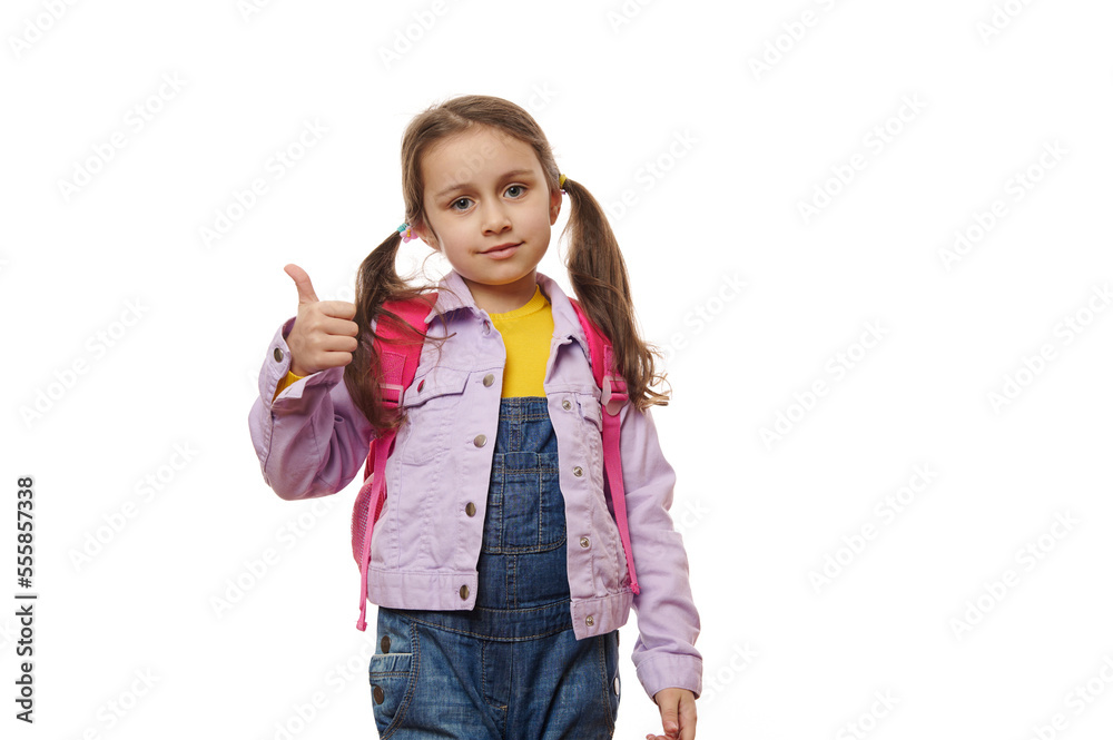 Caucasian adorable little girl, a first grade schoolgirl with backpack, showing thumb up, expressing positive emotions looking at camera, isolated on white background with free advertising space Caucasian adorable little girl, a first grade schoolgirl with backpack, showing thumb up, expressing positive emotions looking at camera, isolated on white background with free advertising space