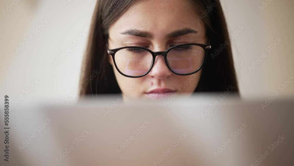 Close-up view of laptop cover and tired eyes of young woman wearing glasses. Portrait of tired woman who working in home freelance office and looks at screen intently. Sadness on hard day at work. Close-up view of laptop cover and tired eyes of young woman wearing glasses. Portrait of tired woman who working in home freelance office and looks at screen intently. Sadness on hard day at work.