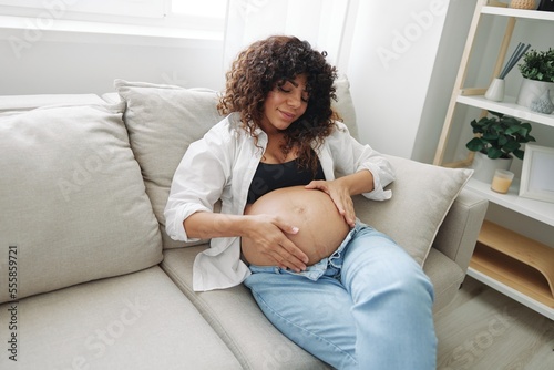 Pregnant woman smile and happiness lies on the couch freedom and strokes her belly with a baby in the last month of pregnancy, mother's day lifestyle