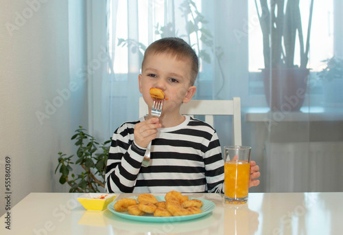 Boy eats fast food at home. Child eats chicken nuggets alone in white kitchen. Harmful  unhealthy food