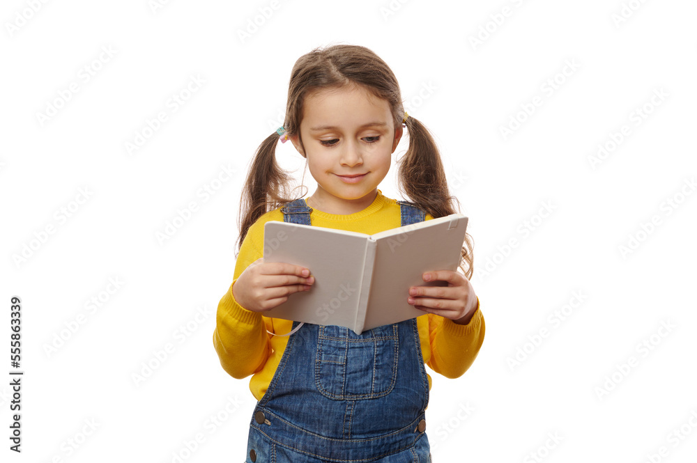 Adorable Caucasian little girl with two ponytails, wearing a yellow pull and blue denim overalls, enjoying reading book over white background. Knowledge Erudition Education Children and School concept Adorable Caucasian little girl with two ponytails, wearing a yellow pull and blue denim overalls, enjoying reading book over white background. Knowledge Erudition Education Children and School concept