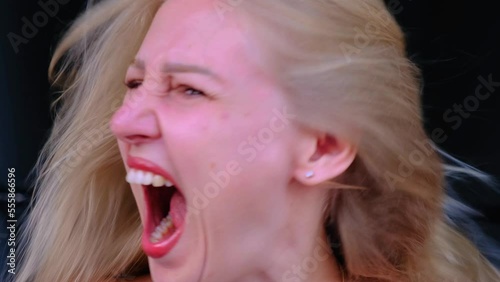 Close-up headshot of blonde woman screaming with her mouth wide open, shaking her head. Woman in difficult emotional state. Hysteria, mental problems. Anger, fear, pain. An overabundance of emotions
