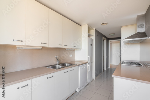 Beige interior of a spacious kitchen with tiled floors  granite countertops with a built-in sink and stove. Light wooden cabinets with crockery. Kitchen has all the necessary appliances.