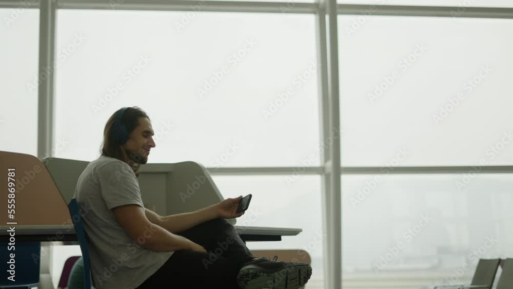 Young handsome long haired man looking at the camera while watching a movie with his mobile phone on an airport Young handsome long haired man looking at the camera while watching a movie with his mobile phone on an airport