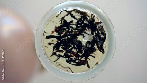 Pouring hot water into a glass with dry tea leaves, Black tea brewing, glass bottom view, close up.
