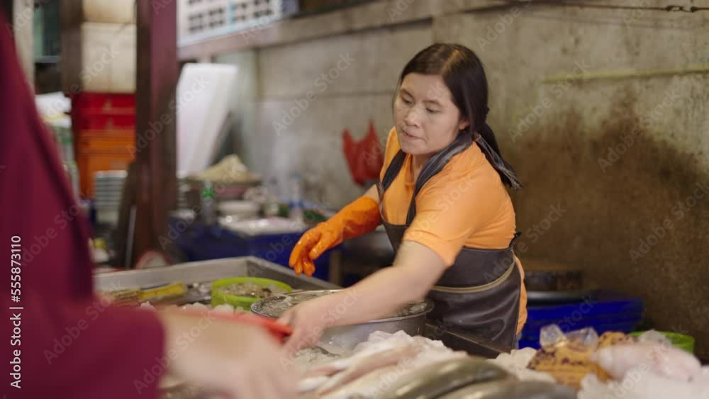 Thai fisher worker weighting seafood with a scale and a plastic basket in Bangkok, Thailand