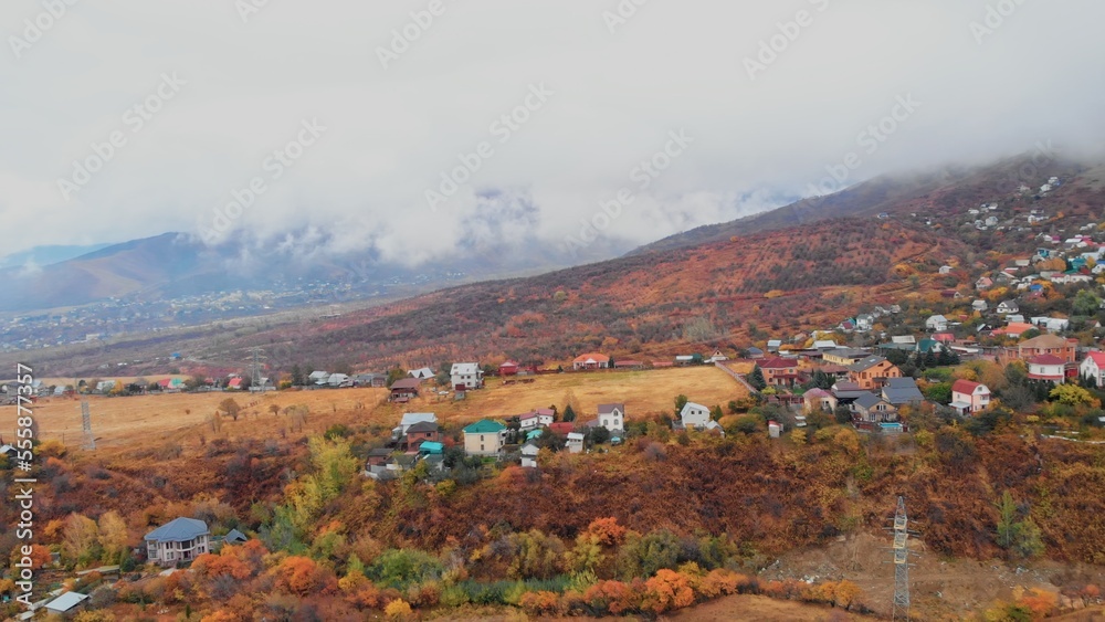 Cinematic view of mountain village in autumn time. Tops of mountains covered with fog at foot of hills are small rural houses. Aerial view of Almaty in autumn. Autumn landscape of an alpine village