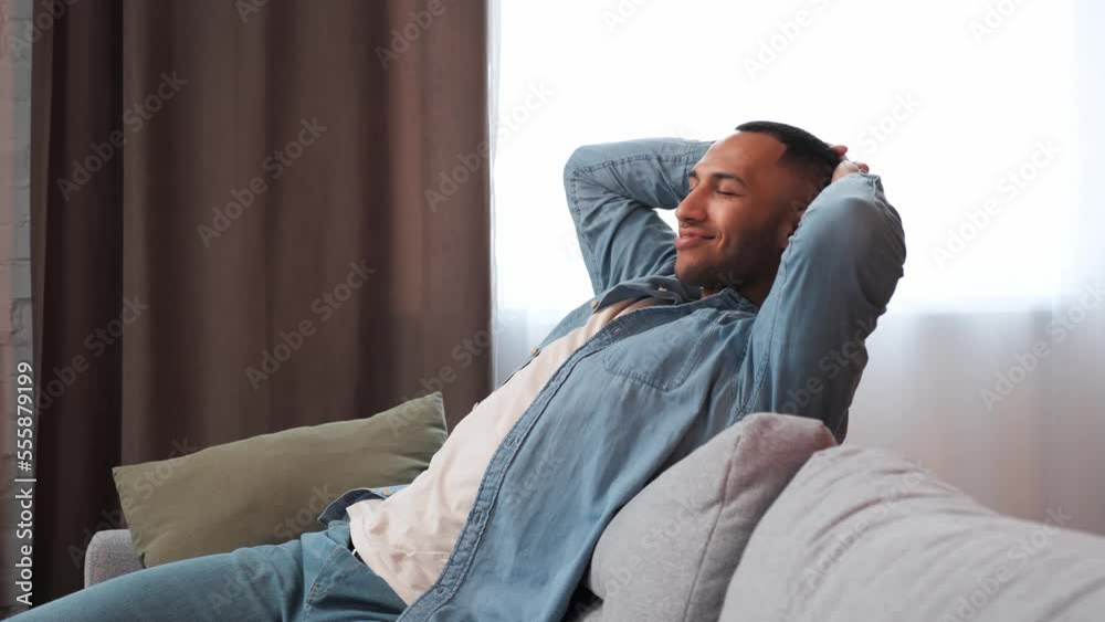 Happy attractive young man resting on couch taking deep breath of fresh air holding hands behind head, satisfied after the work done relaxing on comfortable sofa at home lounge alone. Happy attractive young man resting on couch taking deep breath of fresh air holding hands behind head, satisfied after the work done relaxing on comfortable sofa at home lounge alone.