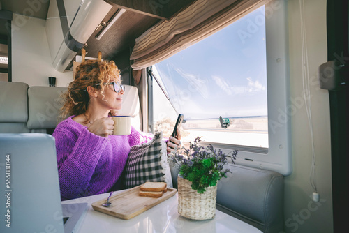 One tourist woman admire the beach inside her modern camper van and use mobile phone. Summer transport holiday vacation people with motor home. Alternative home and lifestyle. Vanlife lady leisure