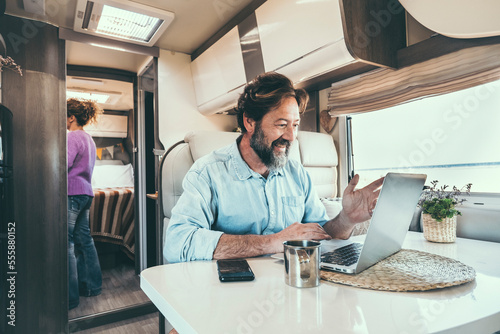 Man and woman living off grid inside a modern camper working on laptop connected online and enjoying freedom and vanlife lifestyle. Happy couple together on travel and vacation. Concept of holiday