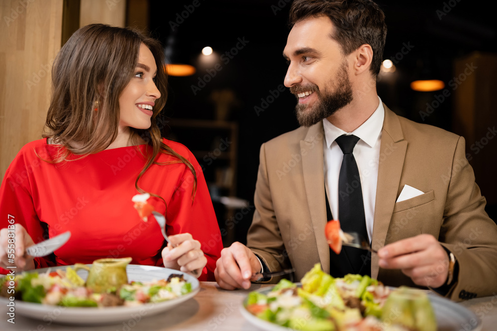 happy young couple in festive attire looking at each other in restaurant during celebration on valentines day