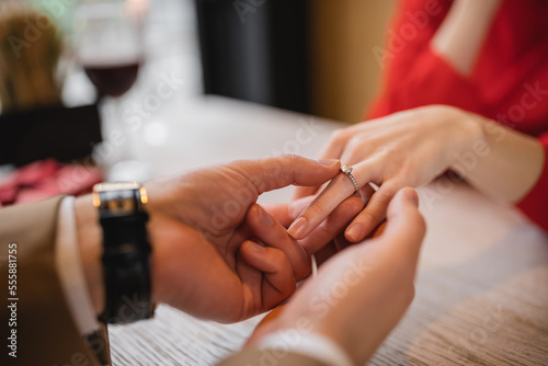 cropped view of man making proposal and wearing engagement ring on finger of girlfriend on valentines day