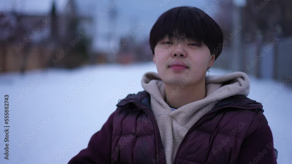 Confident young Asian man looking at camera smiling as live camera zoom out on snowy winter road. Portrait of positive guy in wheelchair posing outdoors on city street Confident young Asian man looking at camera smiling as live camera zoom out on snowy winter road. Portrait of positive guy in wheelchair posing outdoors on city street