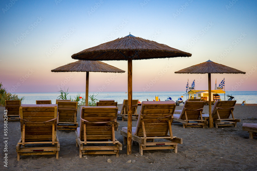 Colorful sky over sunshades with loungers on sandy beach at resort Faliraki in Rhodes island