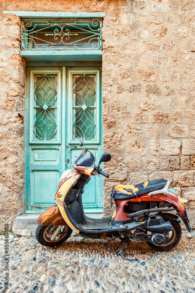 Old moped parked in front of typical mediterranean stone building with blue doors