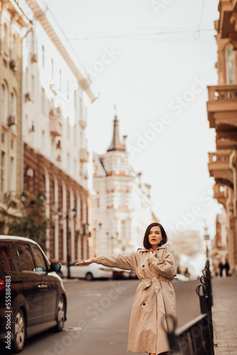 a beautiful brunette woman in a raincoat stops a car on the street of the city.