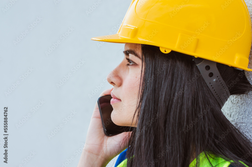 young latin woman engineer in yellow safety helmet outdoors on a phone call, copy space. young latin woman engineer in yellow safety helmet outdoors on a phone call, copy space.