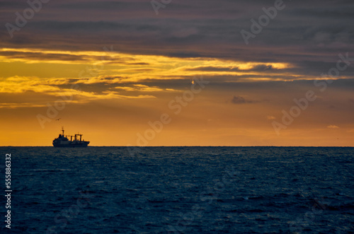 Silhouette of a fishing ship on the horizon of the sea against the backdrop of a dramatic sunset with sunbeams © Max