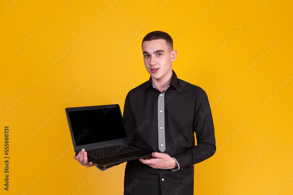 A handsome guy in a black shirt with a laptop on a yellow background A handsome guy in a black shirt with a laptop on a yellow background