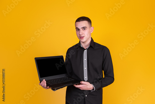 A handsome guy in a black shirt with a laptop on a yellow background