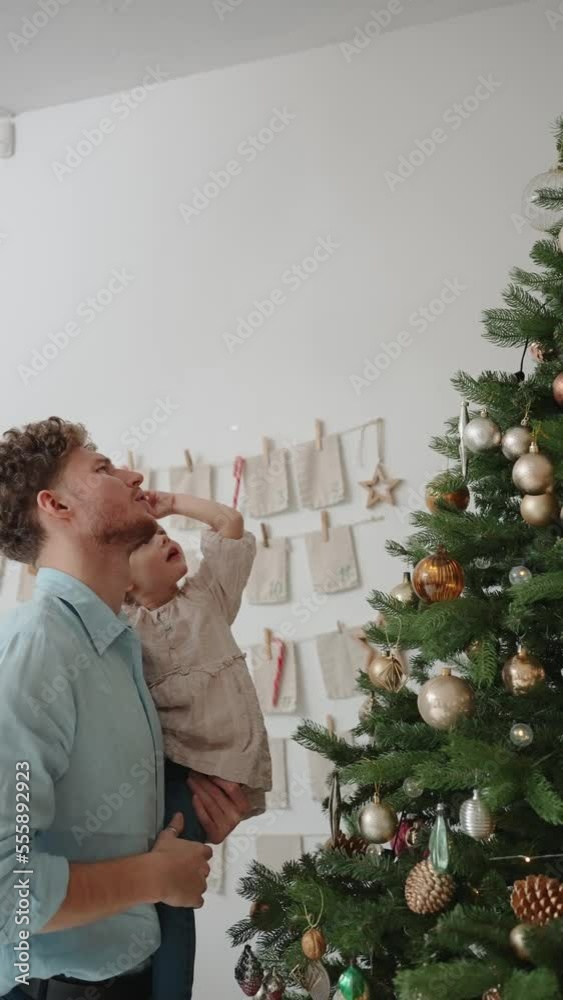 Serious blond father and daughter looking at toys on the Christmas tree at home Serious blond father and daughter looking at toys on the Christmas tree at home