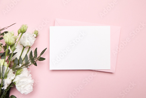 Holiday greeting card mockup with envelope and white flowers on pink background, top view, flat lay. Blank wedding invitation card mockup and floral decor © mikeosphoto