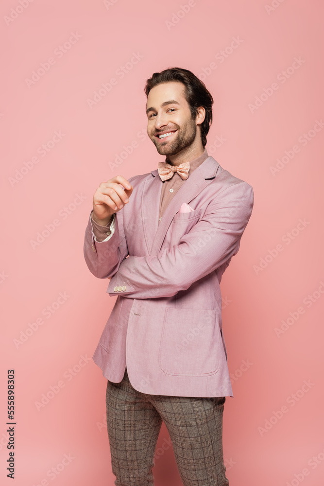 Smiling host of event in jacket and bow tie looking at camera on pink background Smiling host of event in jacket and bow tie looking at camera on pink background