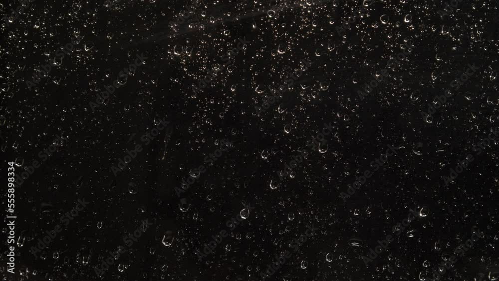 Rainy background. Drops of Night rain water flow down the black glass. The drops are illuminated and sparkle