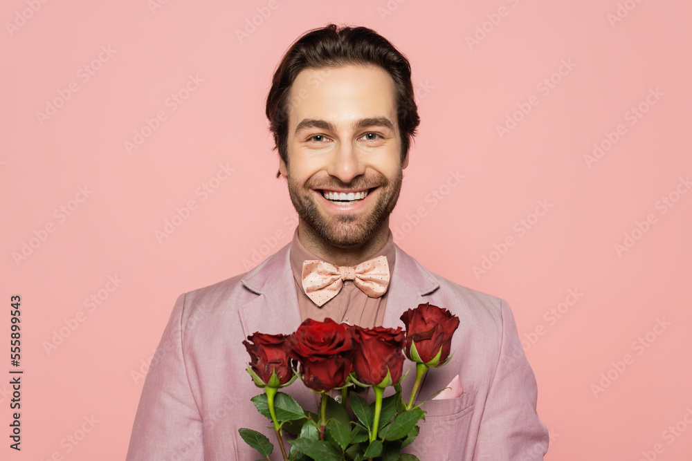 Portrait of positive host of event holding roses and looking at camera isolated on pink Portrait of positive host of event holding roses and looking at camera isolated on pink