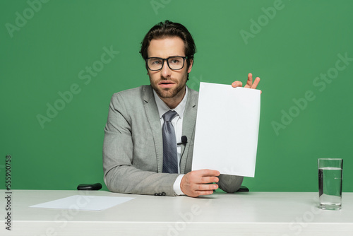 bearded news anchor in eyeglasses and suit holding blank paper isolated on green