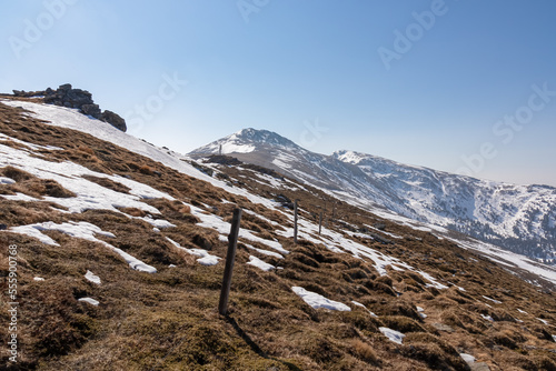 Panoramic hiking trail marked by wooden fence from Hohe Ranach to Zirbitzkogel, Seetal Alps, Styria (Steiermark), Austria, Europe. Snow covered alpine pasture on sunny early spring day. Wanderlust photo