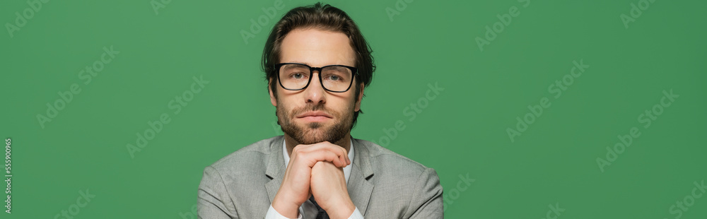 broadcaster in eyeglasses and grey suit with clenched hands isolated on green, banner broadcaster in eyeglasses and grey suit with clenched hands isolated on green, banner