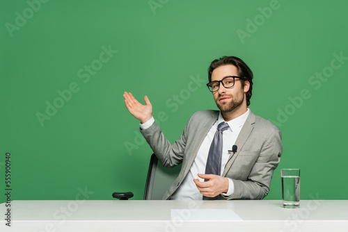Canvas Print broadcaster in eyeglasses and grey suit sitting at desk and pointing with hand i