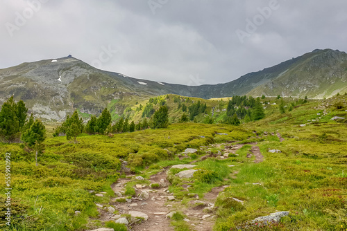 Idyllic trail leading to mountain peak of Zirbitzkogel, Seetal Alps, Styria (Steiermark), Austria, Europe. Landscape of hills, forest, alpine lush green pastures and steep ridges on a cloudy moody day photo
