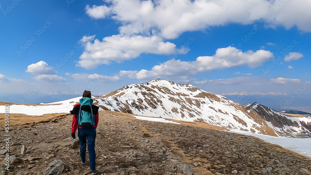 Rear view of woman with backpack looking at snow capped mountain peak Zirbitzkogel and Kreiskogel, Seetal Alps, Styria (Steiermark), Austria, Europe. Hiking trail Central Alps in sunny early spring