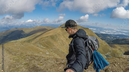 Man with backpack and hat taking selfies with panoramic view of the mountain ranges of Zirbitzkogel Grebenzen, Seetal Alps, Styria (Steiermark), Austria, Europe. Idyllic hiking trails in sunny summer