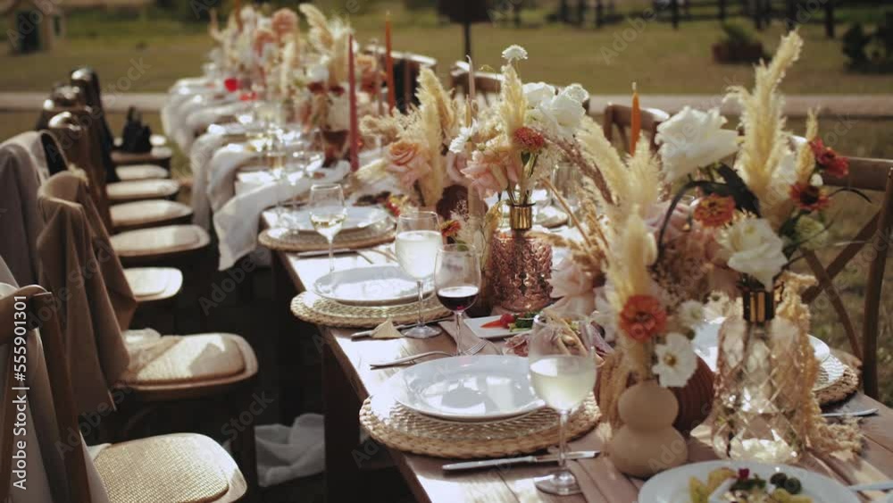 Close-up table served and decorated with candles and dried and pastel flowers for boho style wedding dinner, plates and wne glasses, no people shot, slow motion.