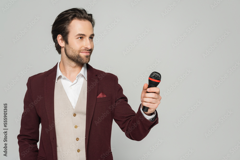 Naklejka premium host of event in red blazer holding microphone isolated on grey