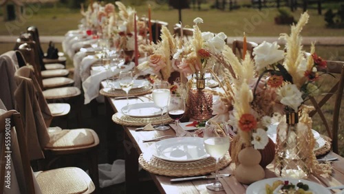 Close-up table served and decorated with candles and dried and pastel flowers for boho style wedding dinner, plates and wne glasses, no people shot, slow motion.